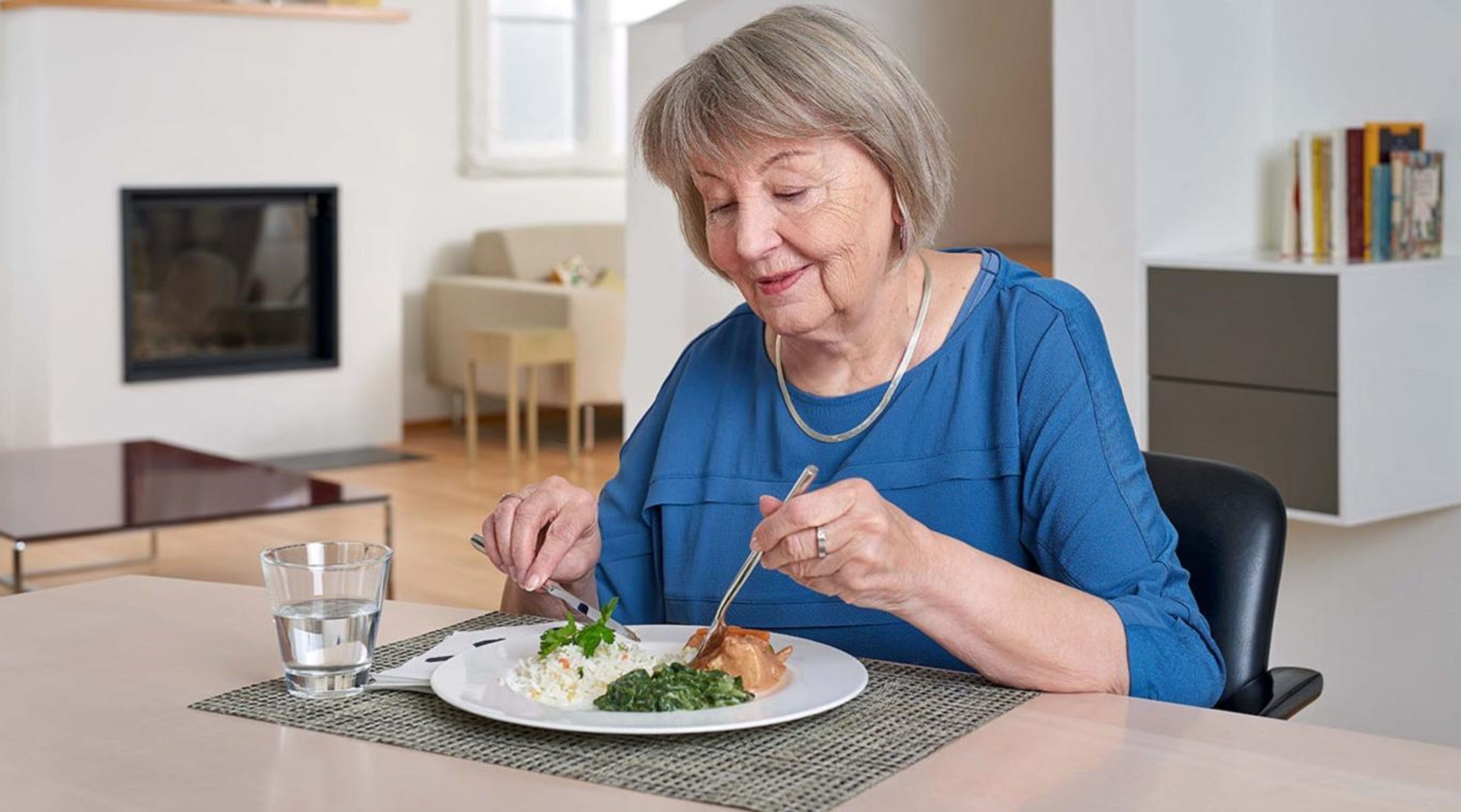 Seniorin sitzt am Tisch und isst ihre Mahlzeit