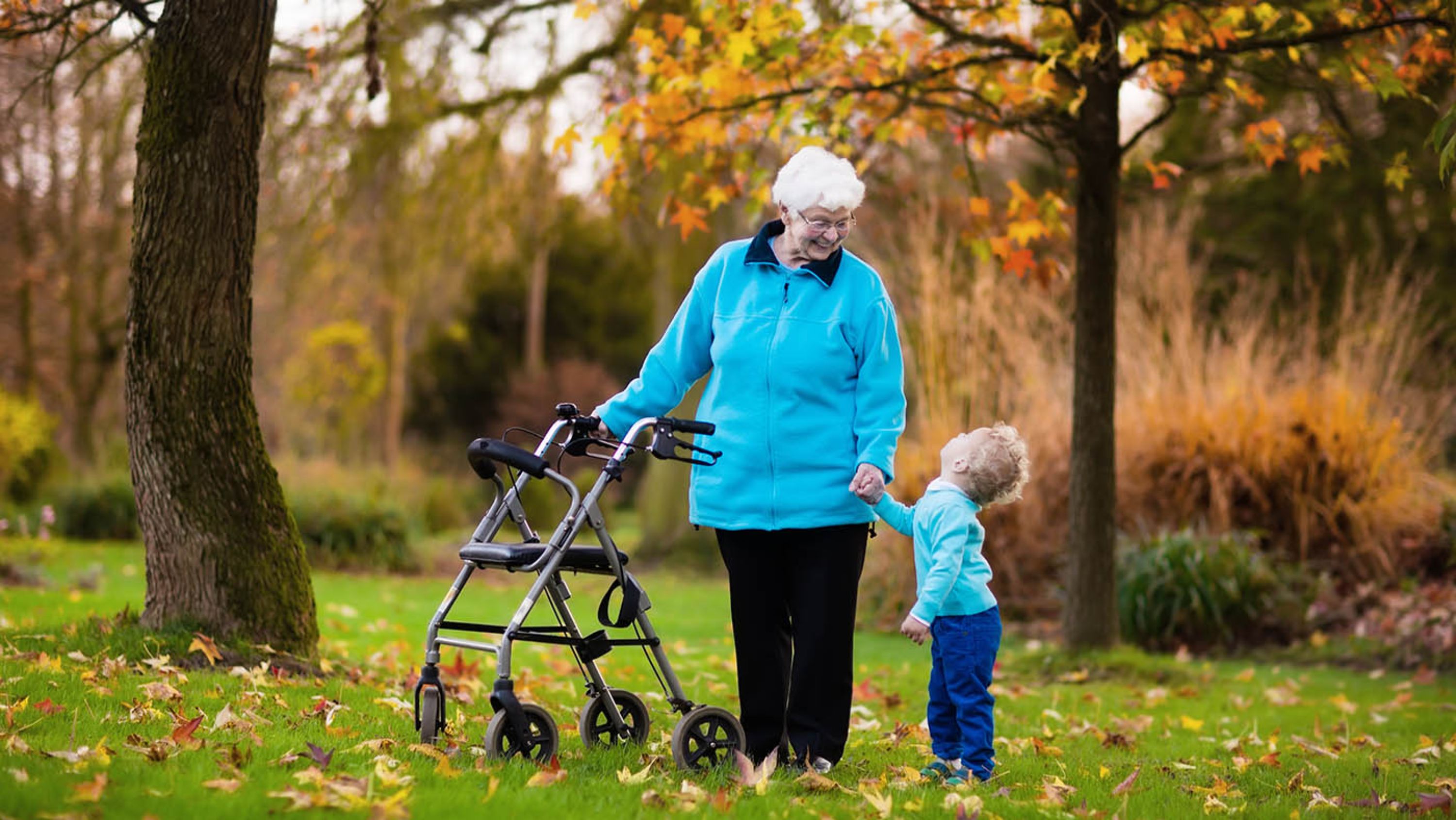 ältere Dame, die sich an Rollator festhält und kleines Kind am Arm hat welches sie lachend anschaut