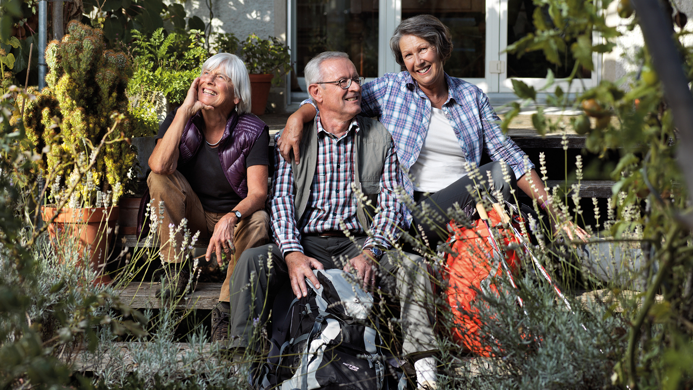 Drei Senioren sitzen im Garten auf einer Treppe und lachen
